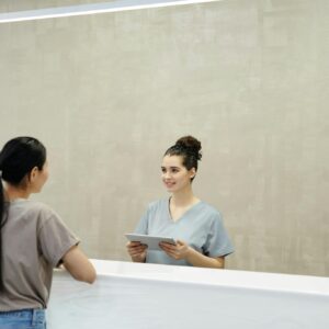 A smiling receptionist with a tablet assists a patient at a medical facility reception desk.