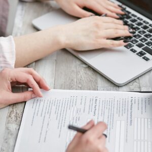Close-up of hands typing on a laptop and reviewing business documents, focused on finance and legal tasks.